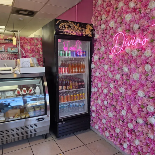 Pared de flores rosadas con r&oacute;tulo de ne&oacute;n junto a la vitrina y la nevera de refrescos