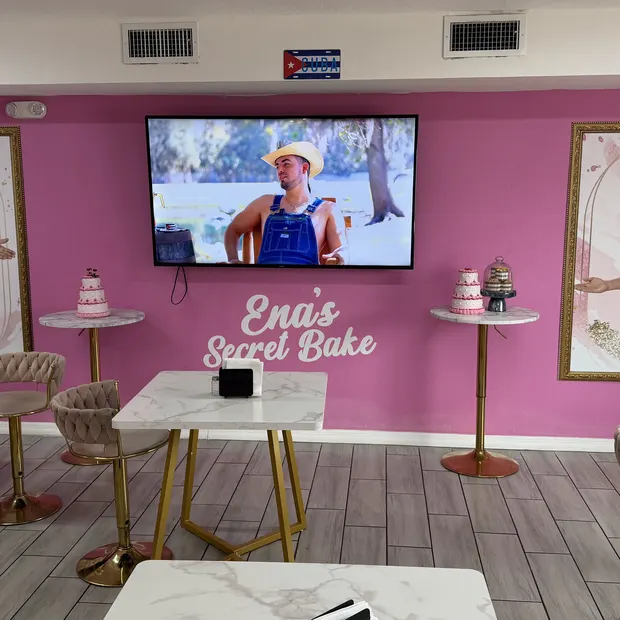 Sal&oacute;n rosado con mesas de m&aacute;rmol, taburetes dorados y los retratos enmarcados en la pared