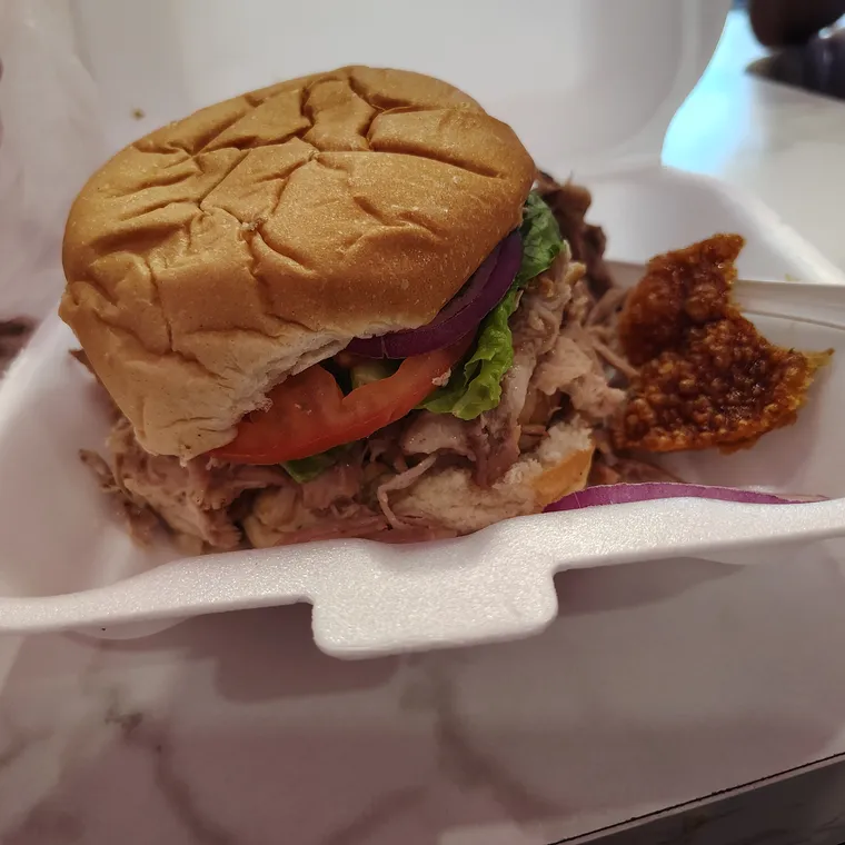 Pan con lech&oacute;n servido en bandeja blanca, con carne desmenuzada, tomate, lechuga y un trozo de chicharr&oacute;n