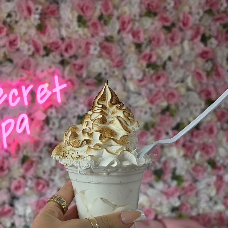 Vaso de merengue tostado sostenido en la mano delante de la pared de flores