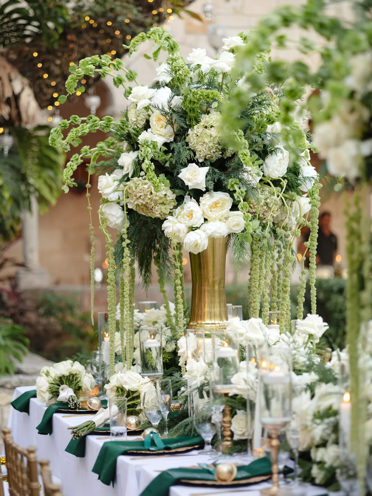 Tall white and green floral arrangement in a gold footed vase on a reception table