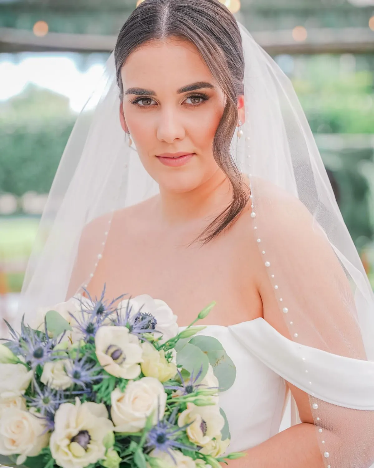 Bride in a pearl-edged veil holding a white and blue bouquet