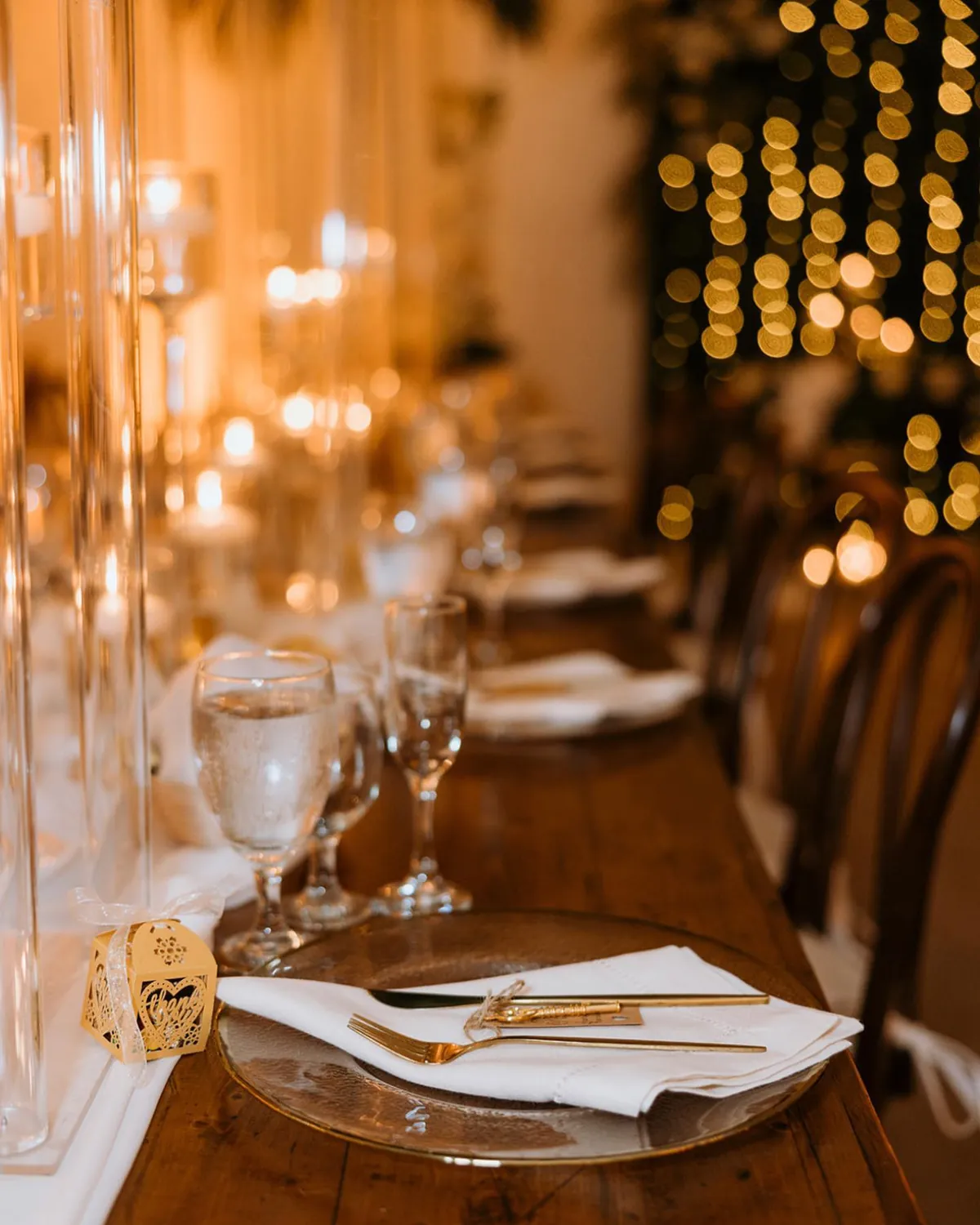Reception table under warm candlelight with gold chargers and folded linen