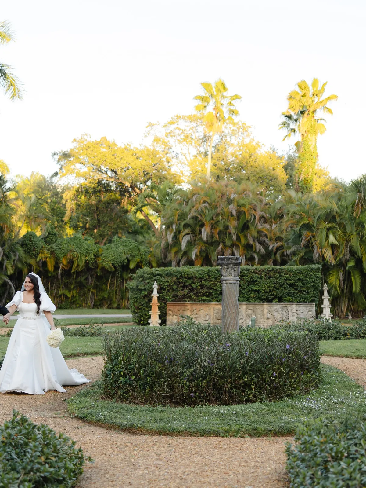 Bride walking through a formal garden in the late afternoon
