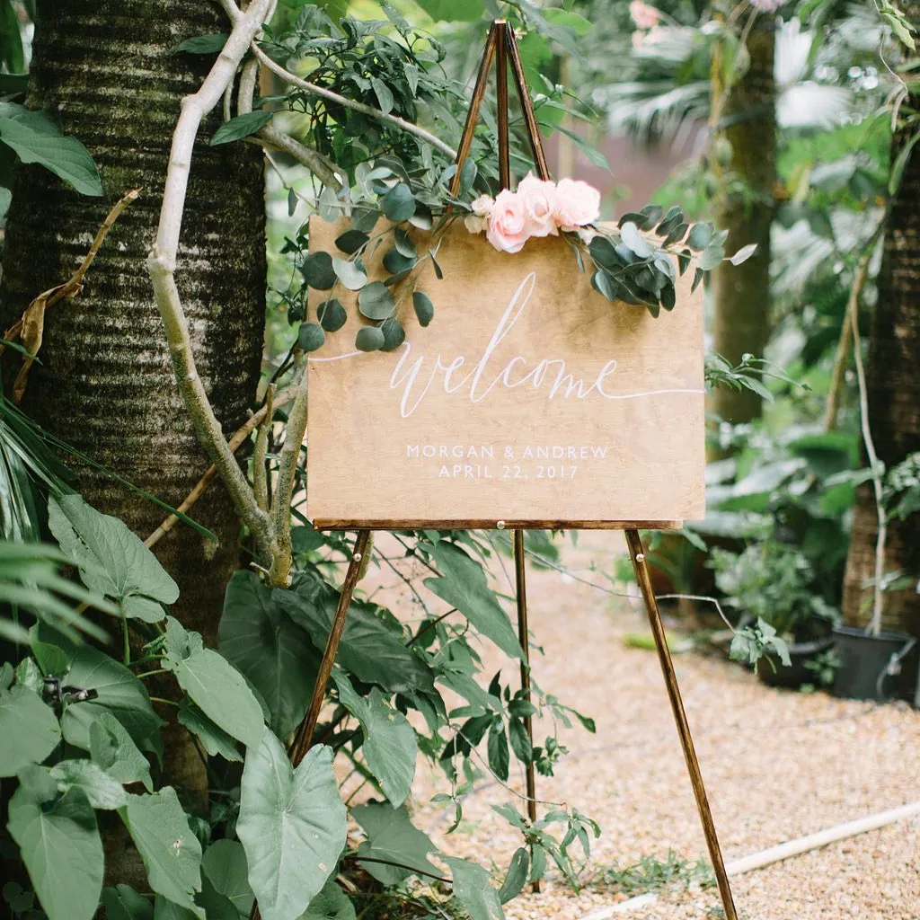 Welcome sign on an easel, dressed with eucalyptus and a pink rose
