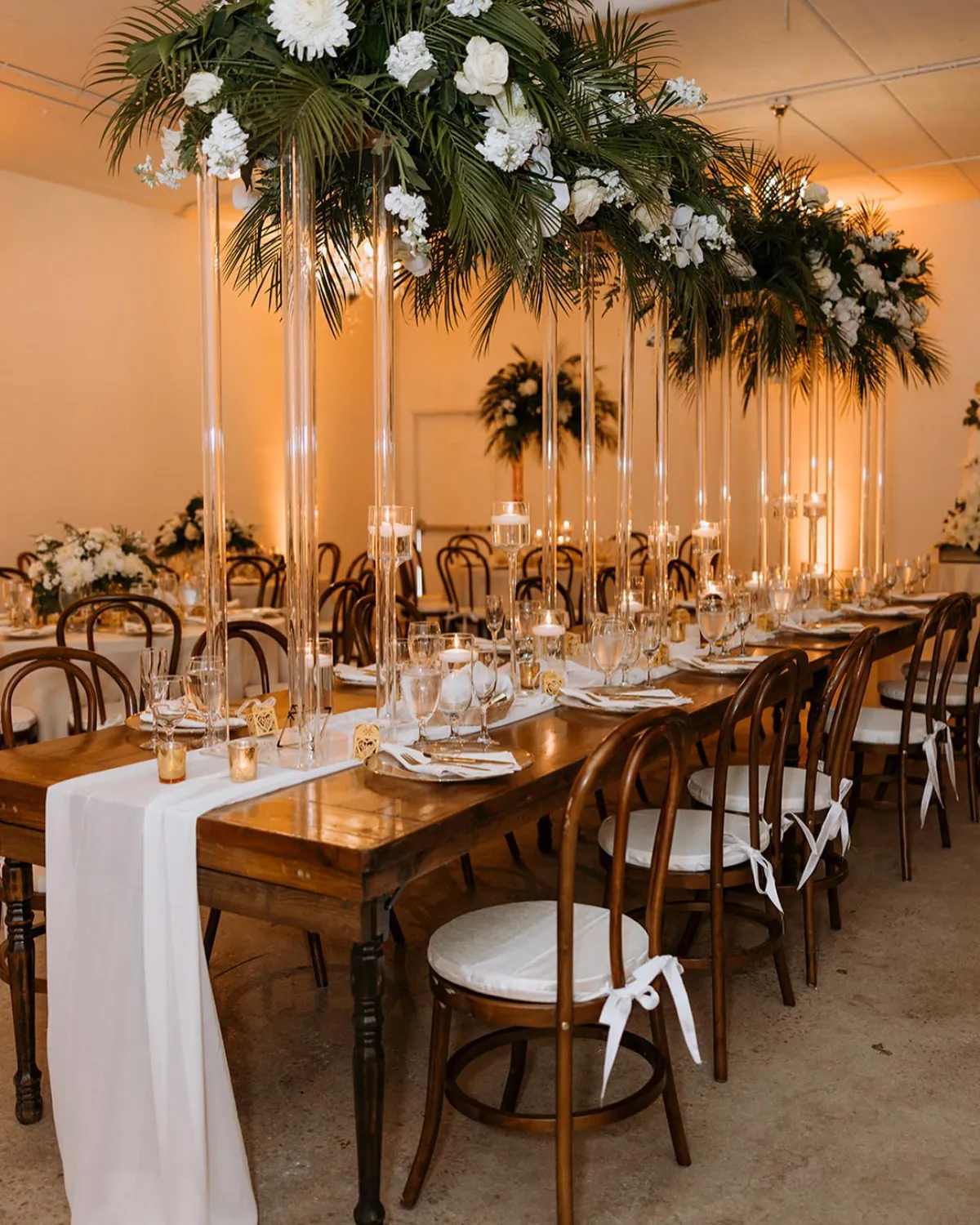 Long reception table with greenery runners, tall arrangements and bentwood chairs