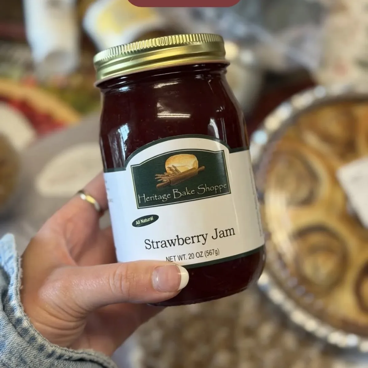 A jar of Heritage Bake Shoppe strawberry jam held in front of the shelves