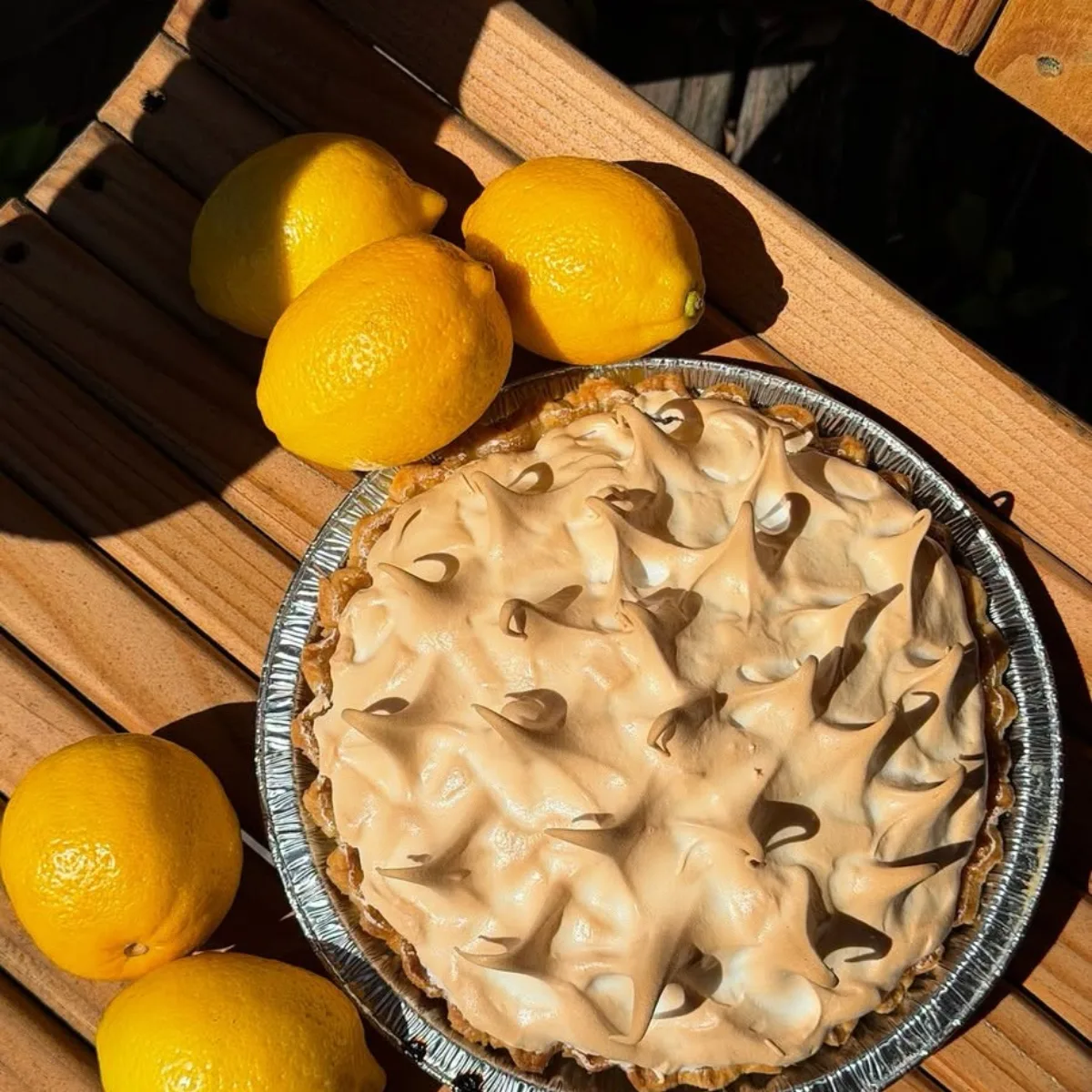 A lemon meringue pie with tall peaks, surrounded by fresh lemons