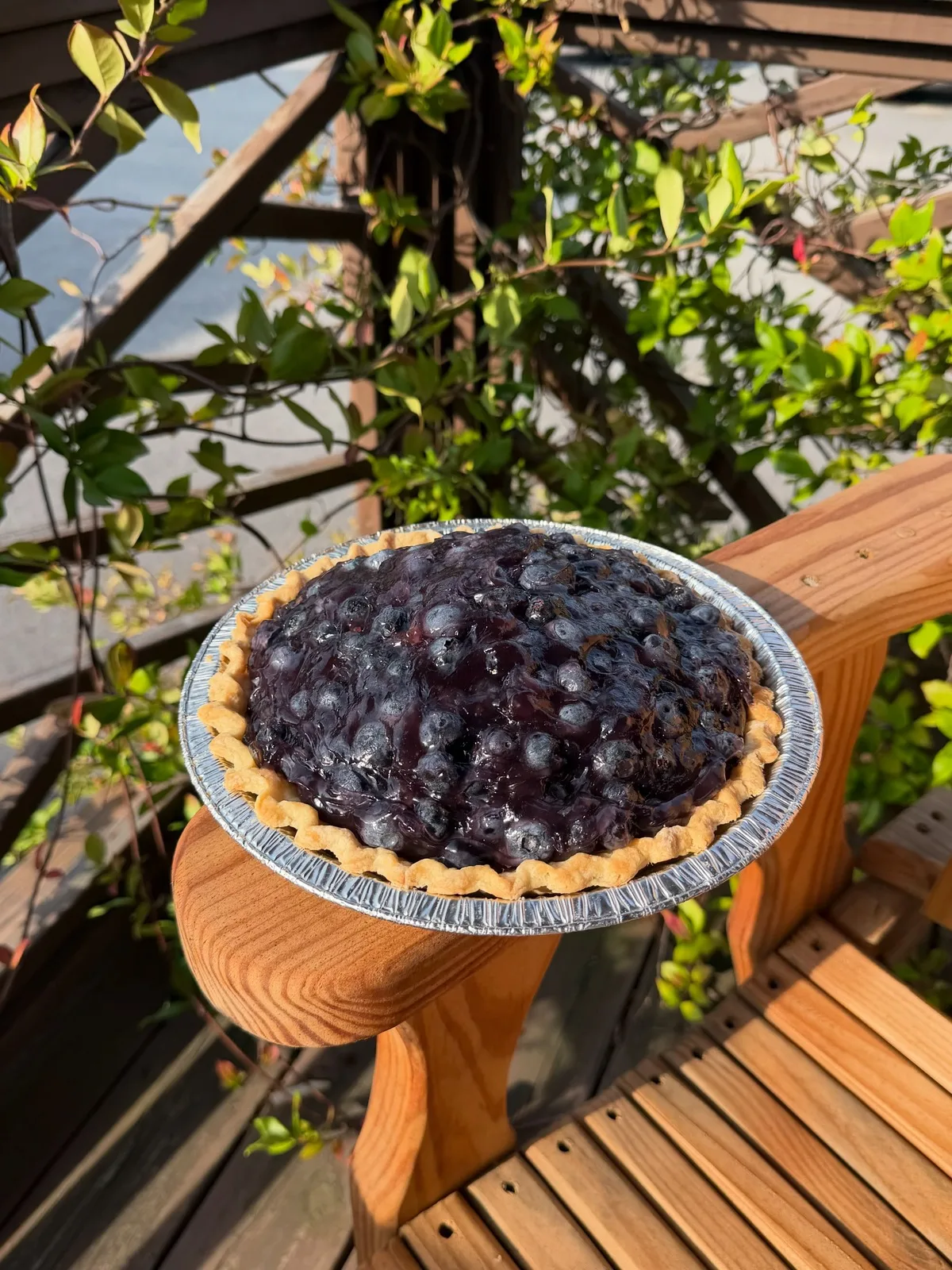 A blueberry pie piled with fresh berries, cooling on a wooden bench outside the shop