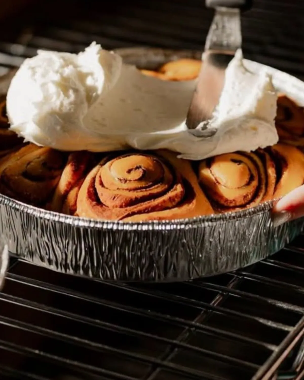 A baker spreading icing over a pan of warm cinnamon rolls