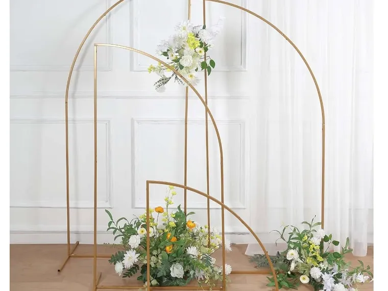 Gold metal arches dressed with white flowers in front of a curtain