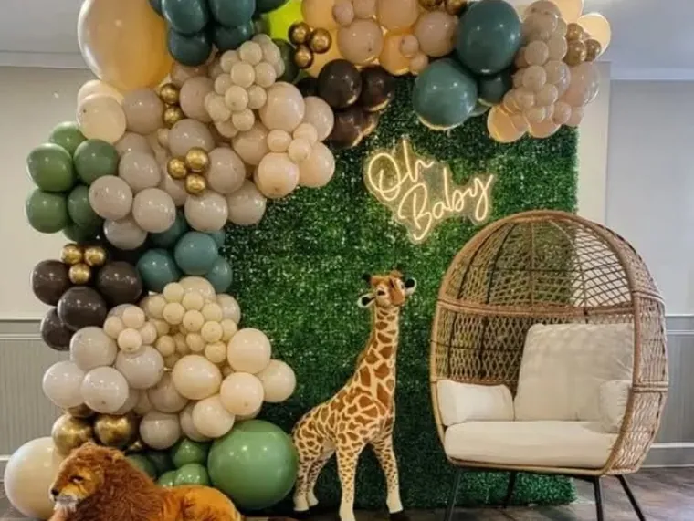 Green and gold balloon garland on a greenery wall with a neon sign