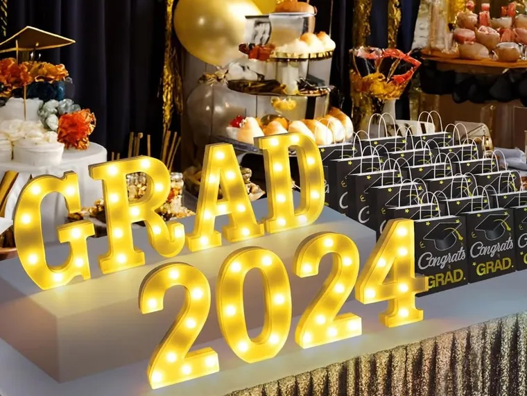 Light-up marquee letters reading GRAD 2024 above a dessert table