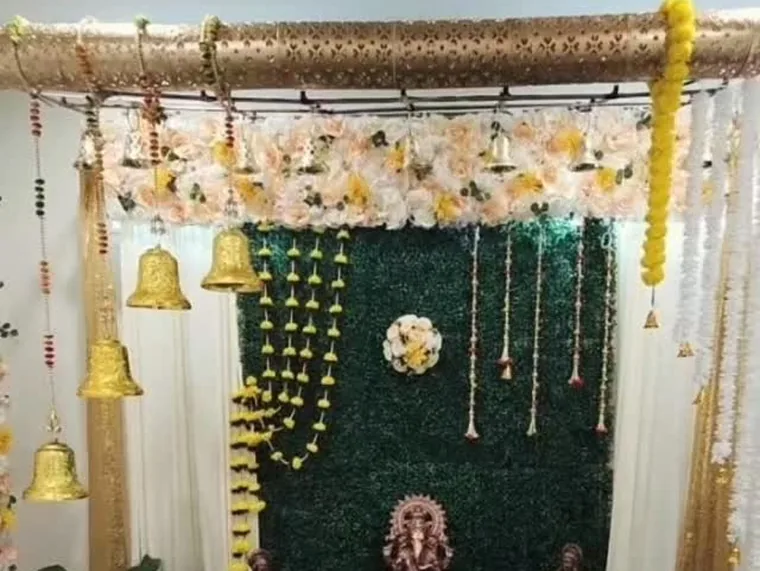 Puja stage with a greenery wall, brass bells and marigold garlands