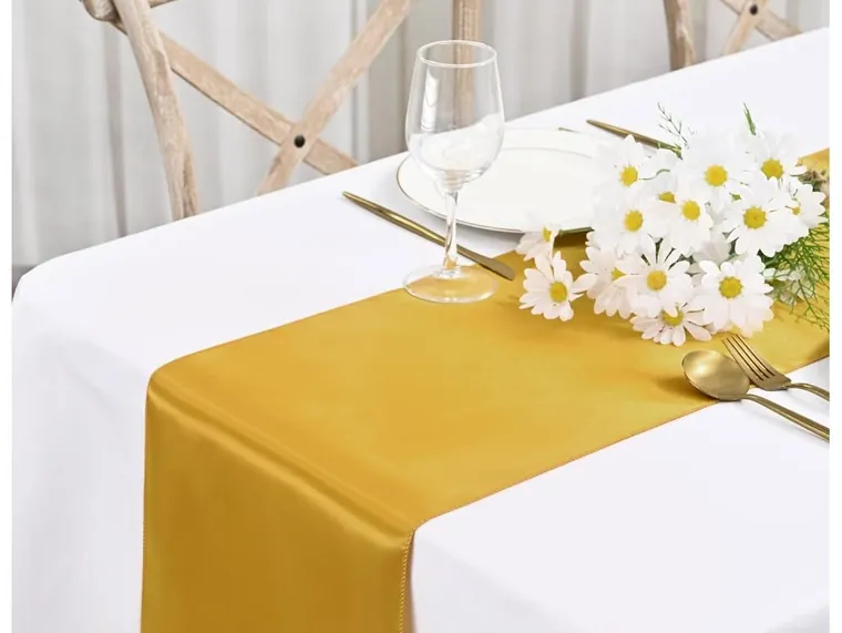 Table set with a gold runner, white cloth and daisies