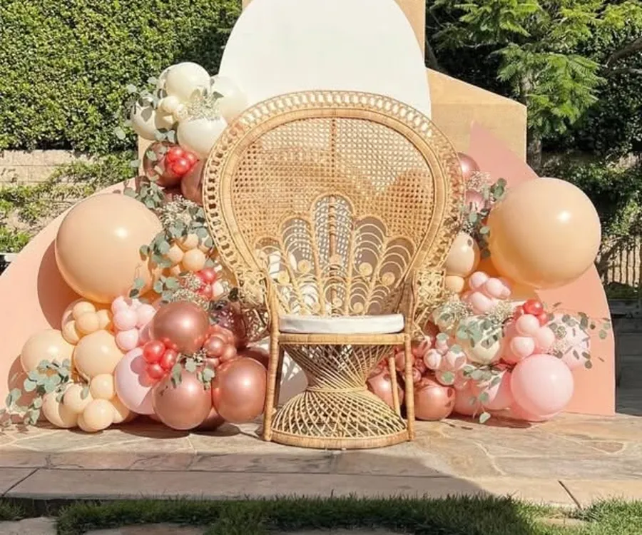 Rattan peacock chair framed by a peach and rose balloon garland