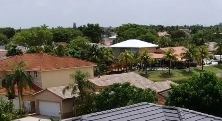 Aerial view of a Hialeah street with tile roofs, palms and a lake behind them.